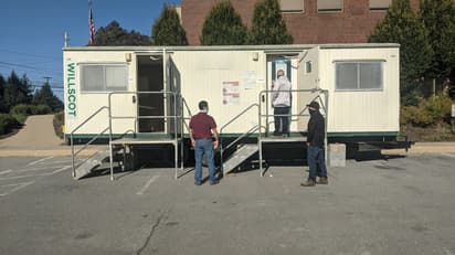Three men wait outside a temperature screening trailer.